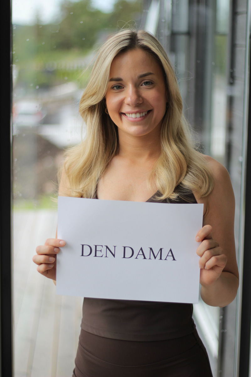 Malin Kristine Moen smiler og holder opp et hvitt skilt med teksten «DEN DAMA».